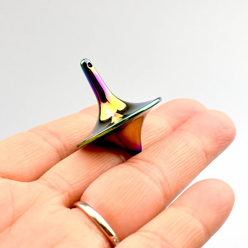A hand holds a metal fidget spinner with iridescent, multicolored finish against a white background.
