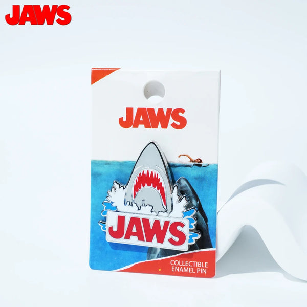 A pack of Jaws collectible enamel pins featuring shark designs and the movie title.