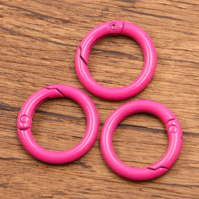 A set of five bright pink metal O-ring spring clasps arranged on a wooden surface.