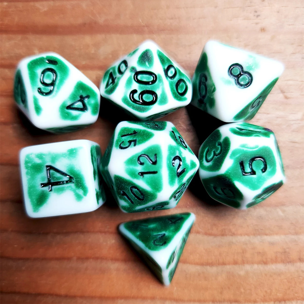 A collection of green and white polyhedral dice scattered on a wooden surface.