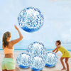 A woman is tossing a blue sequined inflatable beach ball high in the air against a bright sky.