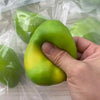 A hand holds a bright green, squishy stress ball with a yellow tint inside clear plastic packaging.