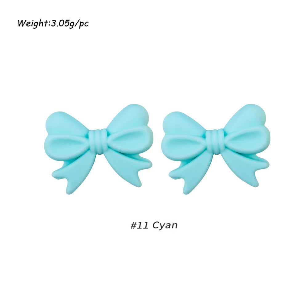 A pair of light blue silicone bow tie beads used for jewelry making and craft projects.