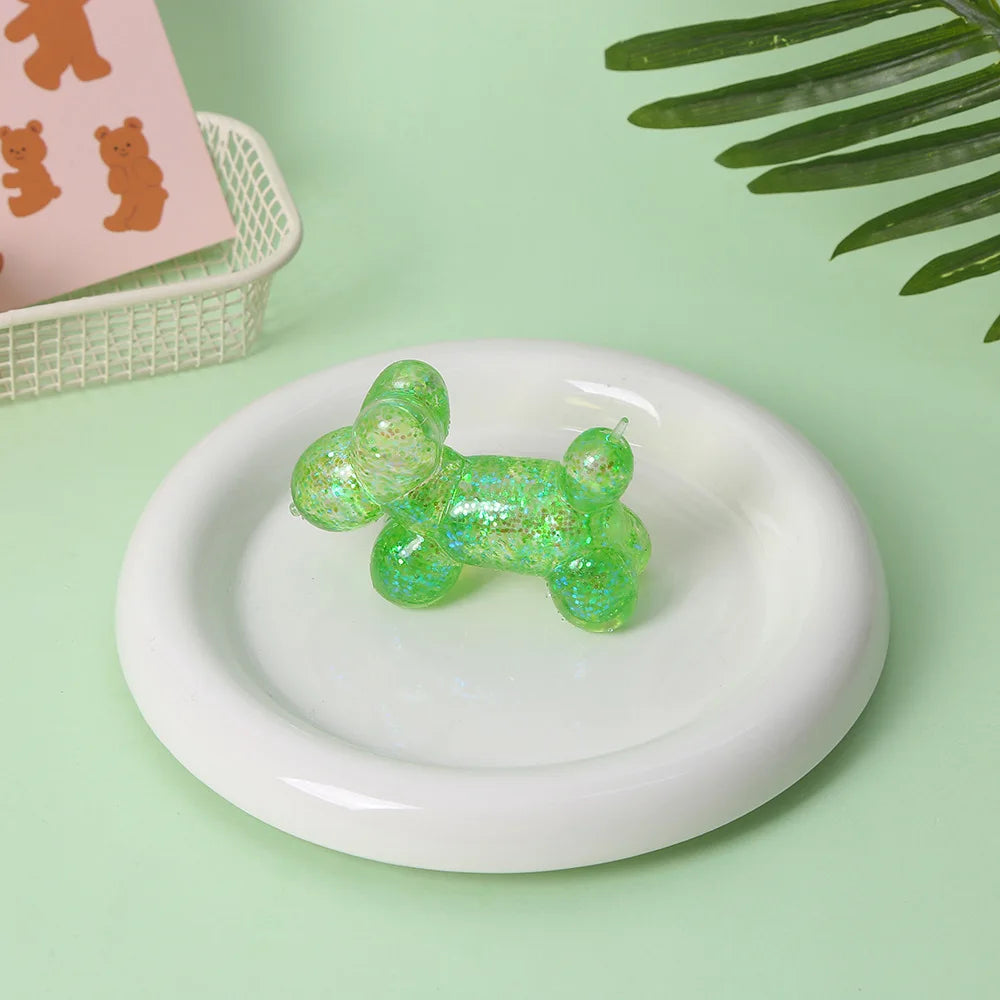 A translucent green squishy toy resting on a white plate with a pink background and a green leaf in the blurred background.