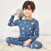 A smiling boy wearing a blue long-sleeved pajama set with an astronaut and lion print, sitting on a white fluffy rug.