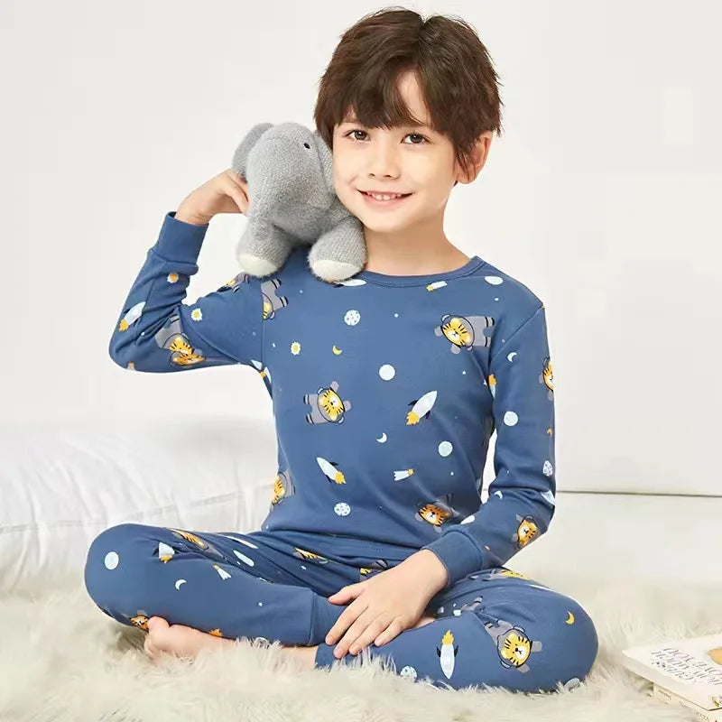 A smiling boy wearing a blue long-sleeved pajama set with an astronaut and lion print, sitting on a white fluffy rug.