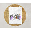 White t-shirt featuring black spooky-themed iron-on patches with purple and orange designs on a woven mat.
