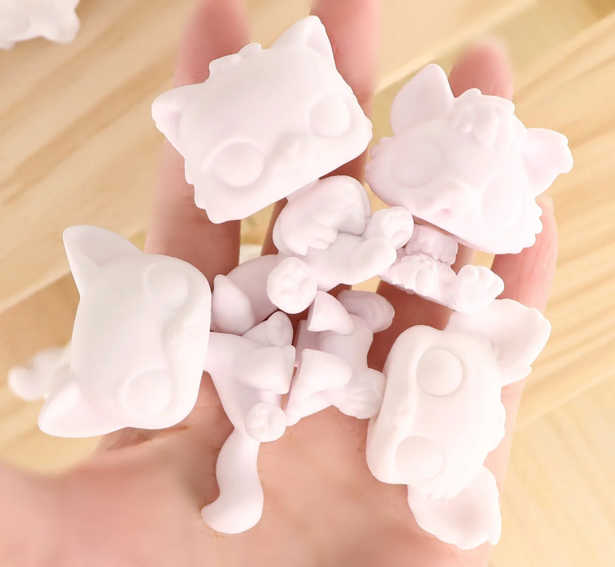 A hand holds a collection of 12 customizable white bobble head pet figures for a DIY kit.