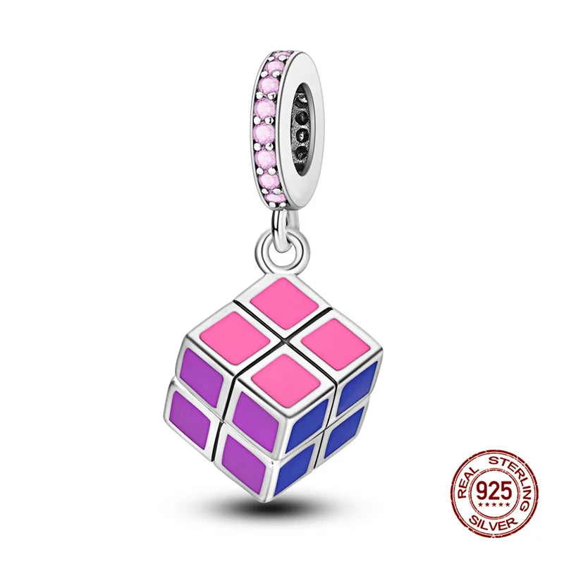 A silver charm shaped like a Rubik's cube with pink and purple facets, featuring a decorative top.