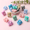 A collection of colorful 3D silicone bear focal beads in various shades of blue, pink, and green arranged on a light backgrou