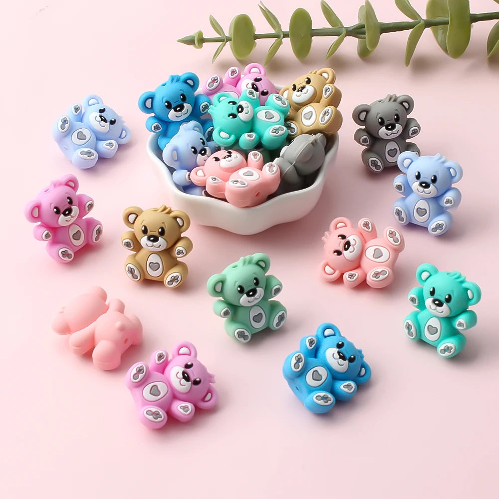 A collection of colorful 3D silicone bear focal beads in various shades of blue, pink, and green arranged on a light backgrou