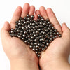 A hand holds a pile of small, round, dark metallic spacer beads for DIY jewelry making.