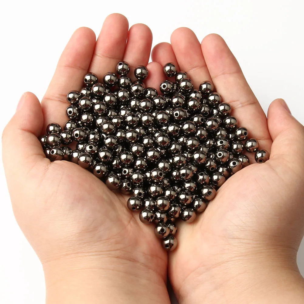 A hand holds a pile of small, round, dark metallic spacer beads for DIY jewelry making.