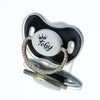 A clear silicone baby pacifier with a black and white design featuring a rhinestone crown and the name Toby.