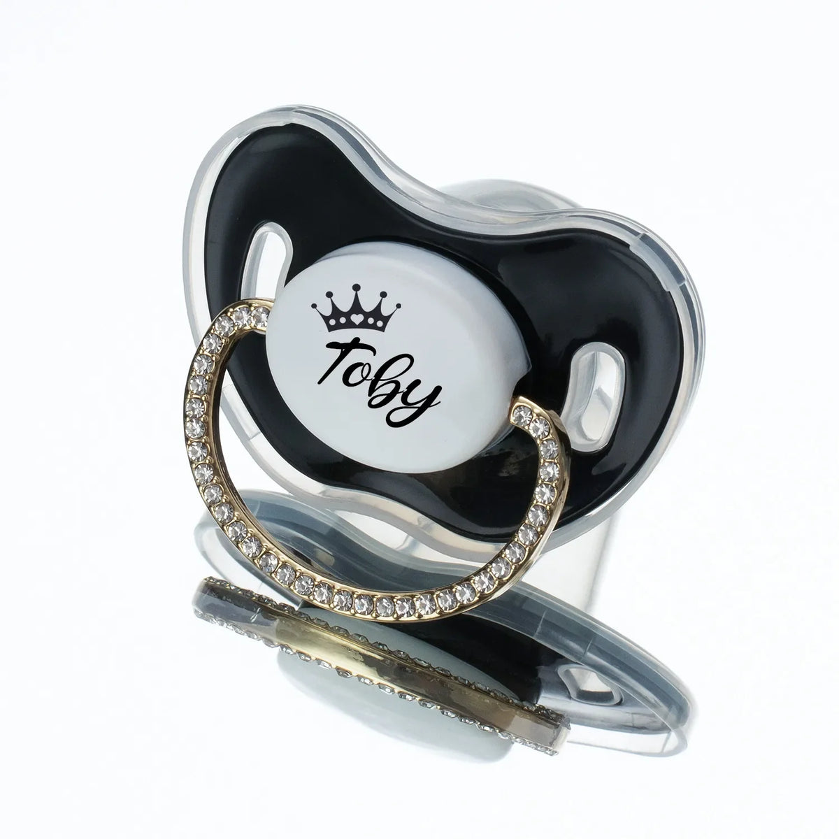A clear silicone baby pacifier with a black and white design featuring a rhinestone crown and the name Toby.