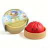 A red dumpling squishy stress ball is shown next to its light brown steamer basket and packaging.
