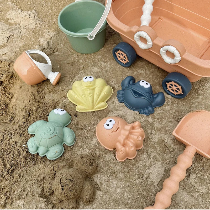 A set of plastic toys including a green bucket, an orange tray, and several green and brown dinosaur-like figures on sand.
