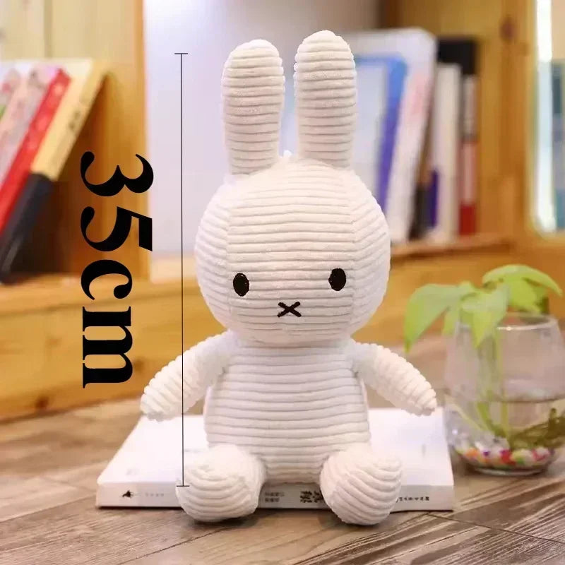 A white Miffy plush toy with long ears is shown standing on a wooden surface.