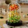 A glass terrarium containing a miniature plant with orange and yellow flowers.