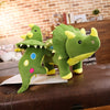 A green dinosaur plush toy with yellow accents is displayed on a brown leather surface.