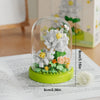 A clear glass dome containing a miniature flower bouquet made of green and white building blocks.