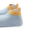 A pair of light blue knitted socks with tan cuff and non-slip grips shown from the side.