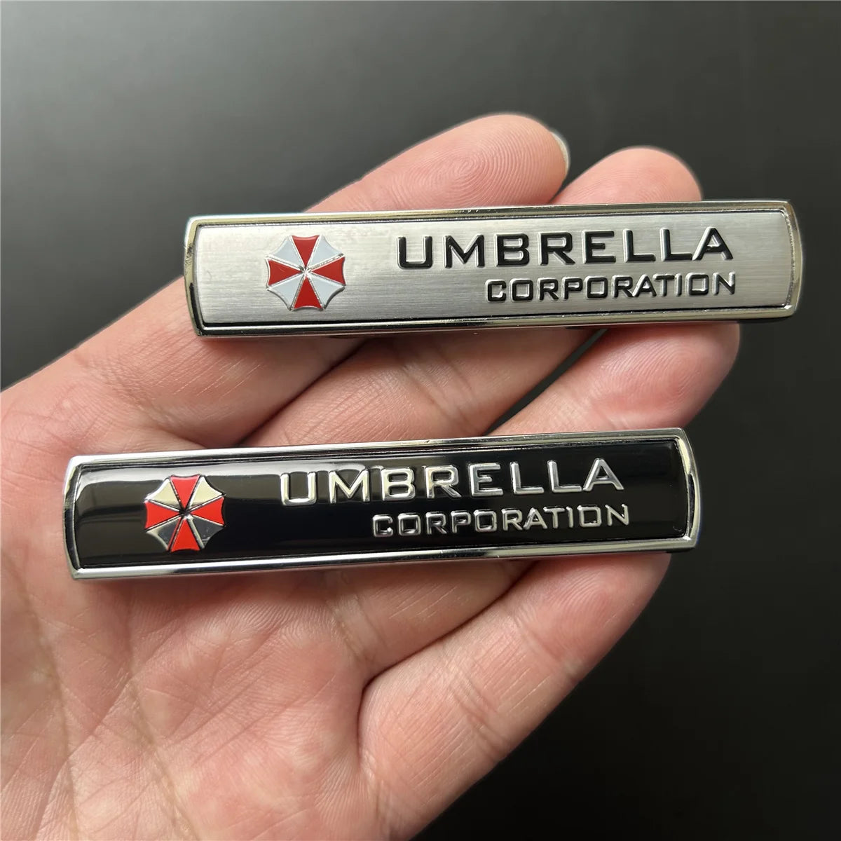 A hand holds a silver and black metal emblem badge for Umbrella Corporation.