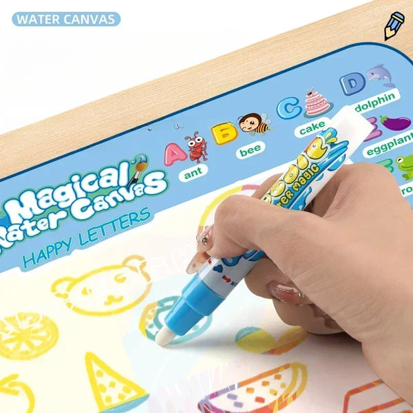 A hand is drawing letters on a Magic Water Canvas mat with a paintbrush, showing colorful letters and fruit shapes.