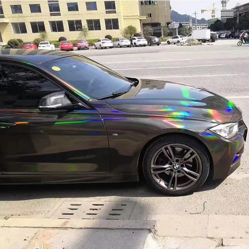 A dark green BMW is shown with a holographic chrome vinyl wrap finish parked on an asphalt street.