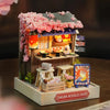 A detailed wooden miniature dollhouse kit featuring a pink flower shop facade and various small wooden accessories.