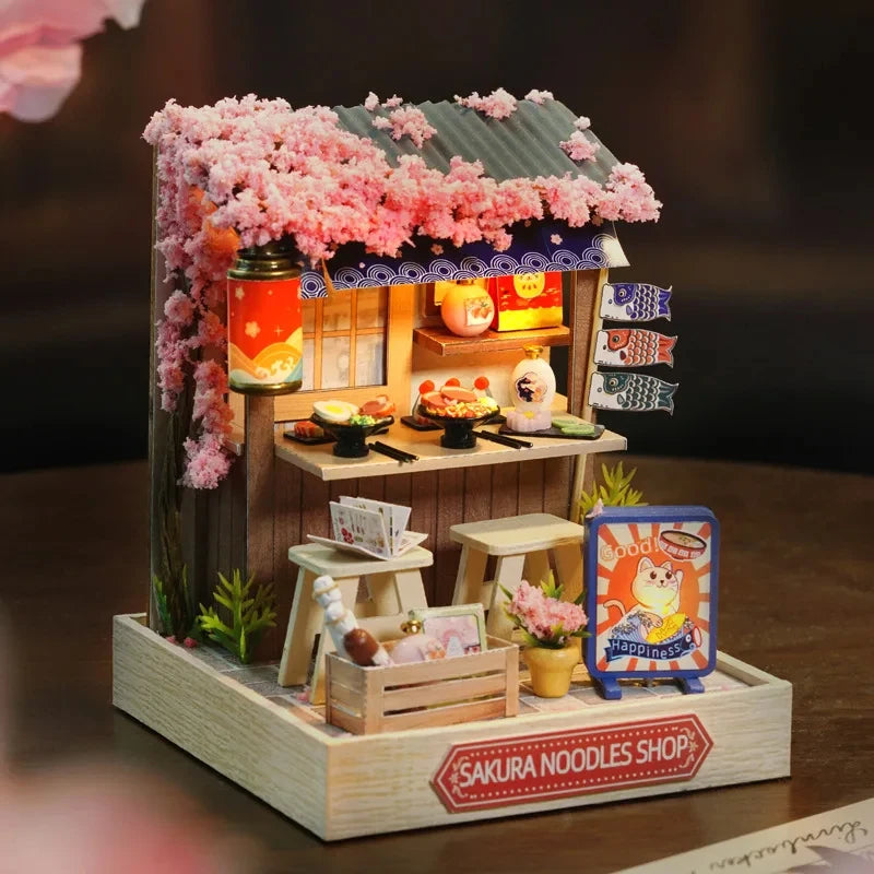 A detailed wooden miniature dollhouse kit featuring a pink flower shop facade and various small wooden accessories.