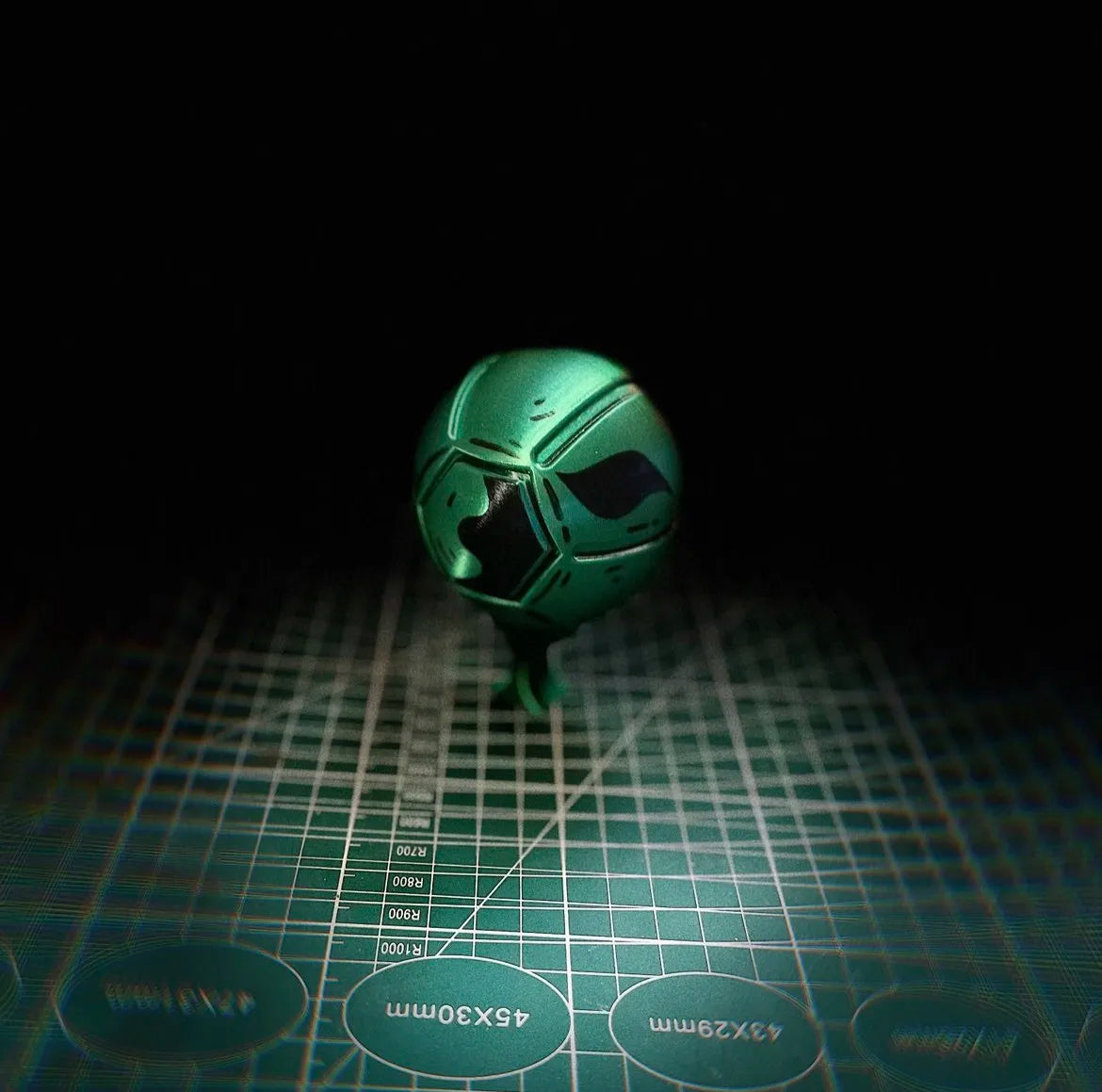 A green steel ball fidget toy with a black section, resting on a grid surface.