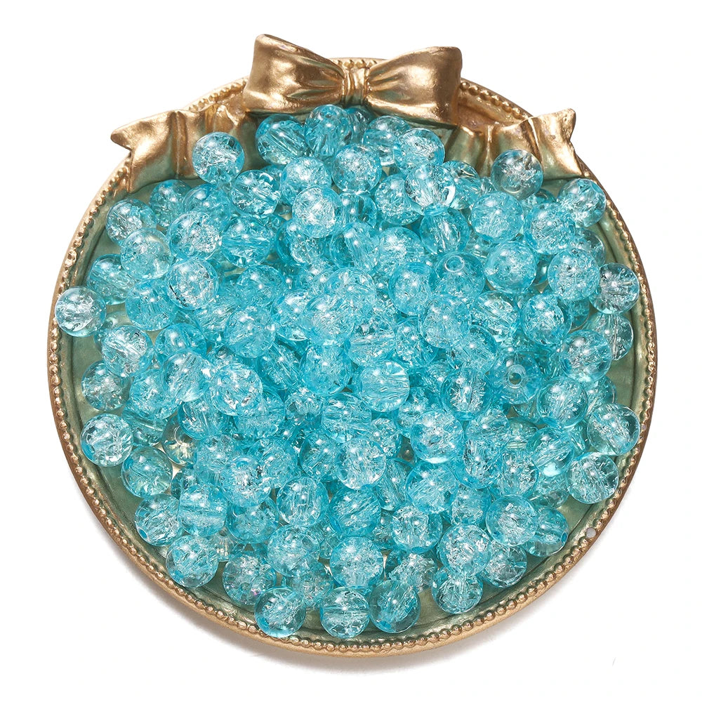A round dish filled with clear blue glass crackle beads tied with a gold bow for jewelry making