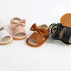 A collection of baby summer sandals in various colors including white, pink, brown, and black with bowknot details.