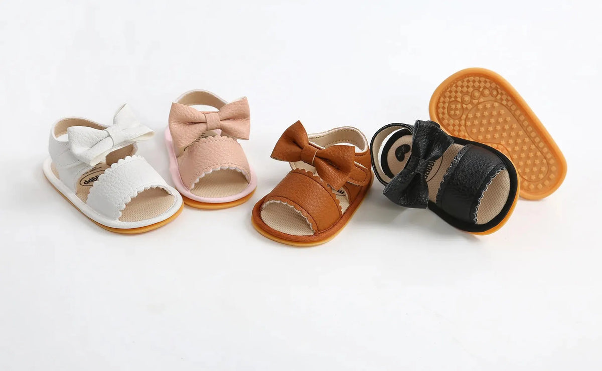 A collection of baby summer sandals in various colors including white, pink, brown, and black with bowknot details.