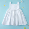 A white summer cotton linen jumper dress for a toddler girl displayed against a light blue background.