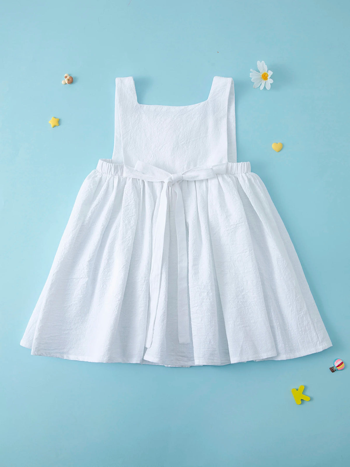 A white summer cotton linen jumper dress for a toddler girl displayed against a light blue background.