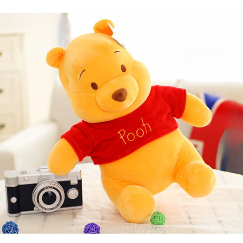 A yellow Winnie the Pooh plush toy wearing a red shirt is shown next to a camera.