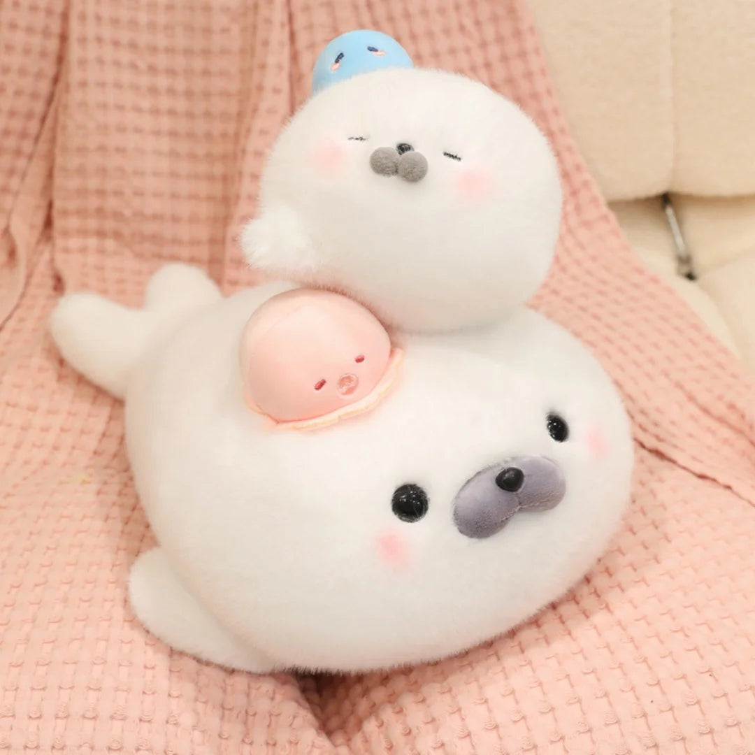A white seal plush toy with a light pink octopus hat resting on a pink knitted fabric.