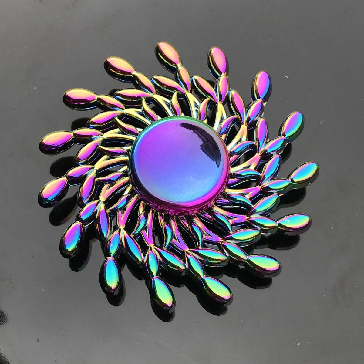 A close-up of a rainbow metal fidget spinner with a smooth, iridescent purple center and surrounding metal blades.
