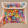 A clear plastic bag filled with a multi-pack of colorful nylon hair ties in various shades of pink, blue, yellow, and orange.