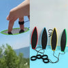 A hand is shown holding a green mini surfboard skateboard toy with black and yellow fins, next to several black rubber rings.