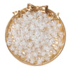 A round gold-rimmed dish filled with clear glass crackle beads for jewelry making
