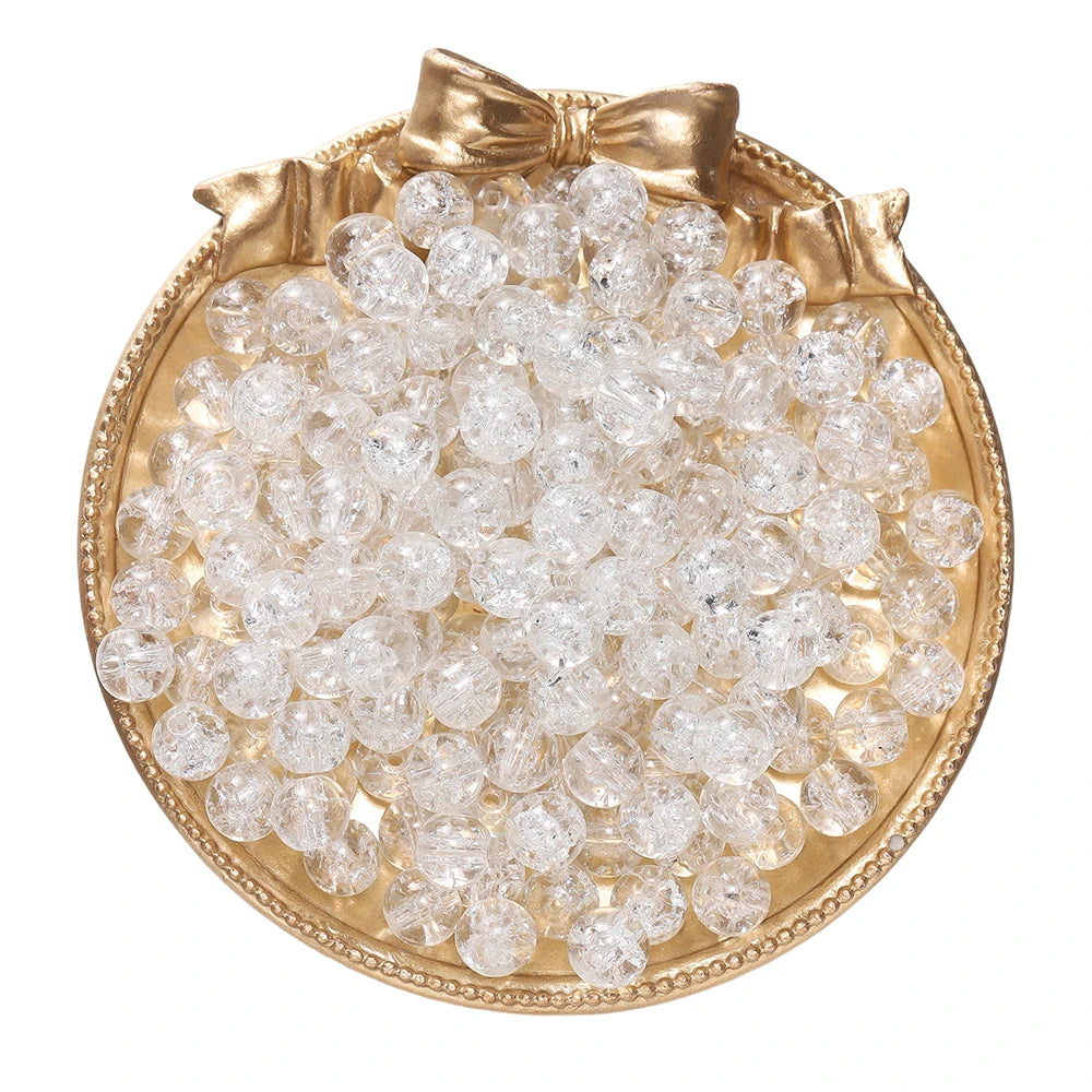 A round gold-rimmed dish filled with clear glass crackle beads for jewelry making