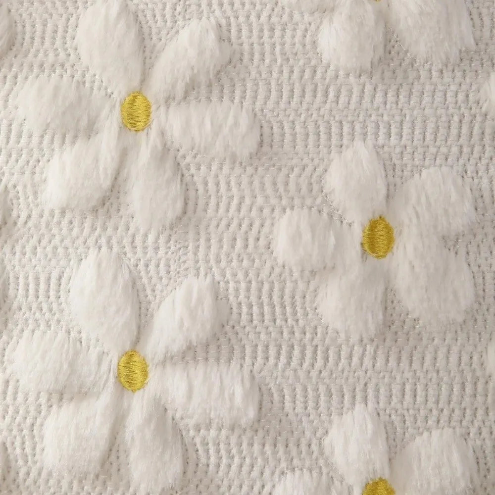 White faux fur pillow covers featuring embroidered yellow daisy designs on a textured fabric.