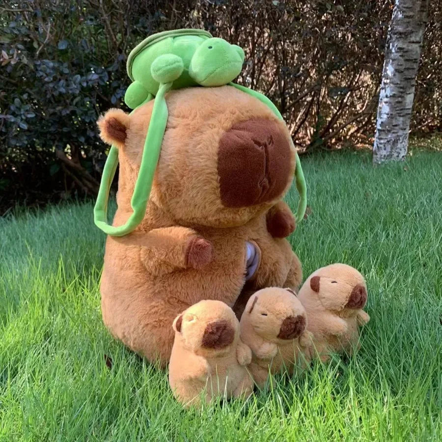 A brown capybara plush mother with four small baby capybaras lying in green grass.