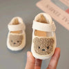 A pair of adorable bear soft sole first walker shoes for babies in cream color being held by a hand.