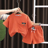 An orange boys' summer cotton t-shirt and shorts set displayed on a hanger against a dark curtain.