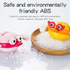 A yellow wind-up swimming bath toy animal is shown next to a pile of clear bath salts on a wooden surface.