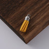 A brass tassel with yellow velvet fibers is displayed on a dark wooden surface.